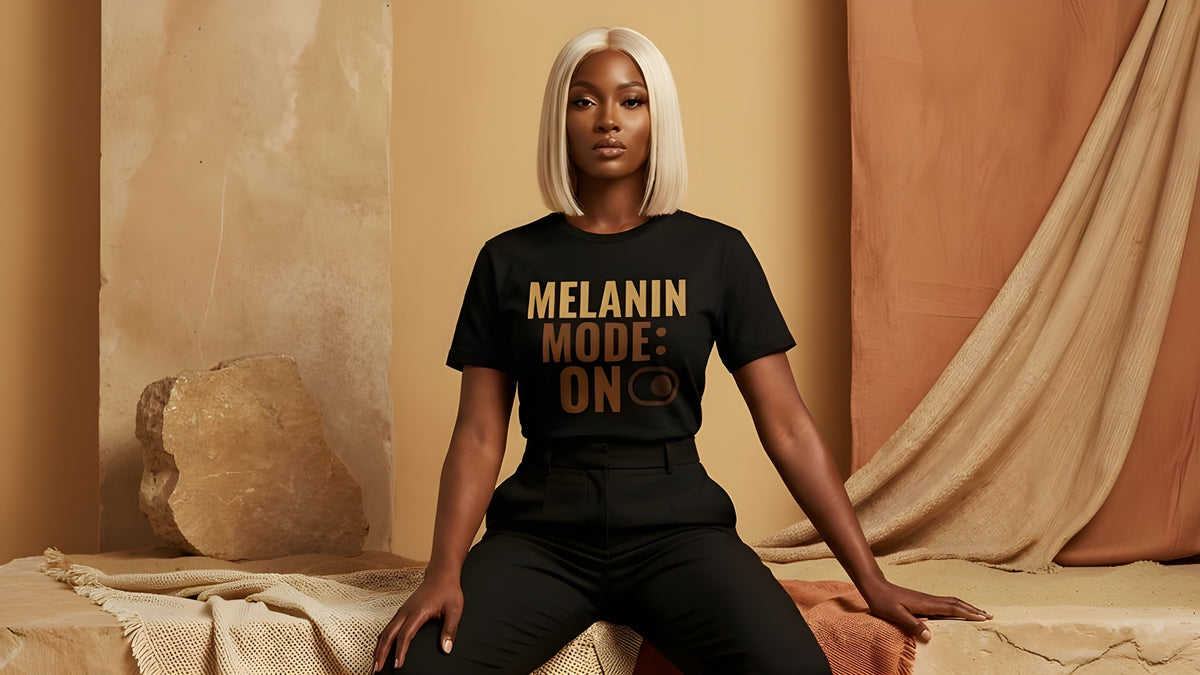 Black woman wearing a black t-shirt with 'Melanin Mode: On' text in a warm-toned room.